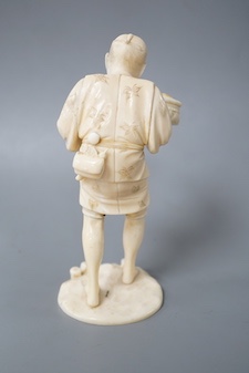 A Japanese carved ivory figure, Meiji period, modelled as a fruit vendor carrying a bowl of fruit in one hand and a piece of fruit in the other, standing on a naturalistic circular base, signed on base, height 14.5cm